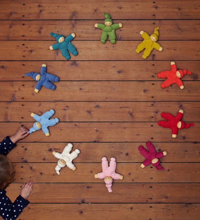 The Nanchen Waldorf Pimpel dolls in a circle, with a child playing with a light blue on in the bottom left hand corner