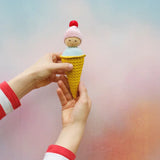 Adult hands holding Nanchen ice cream rattle doll  against a pastel background. Doll fits nicely in the hand
