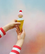 Adult hands holding Nanchen ice cream rattle doll  against a pastel background. Doll fits nicely in the hand