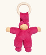 Nanchen Pimpel Doll Baby Comforter in berry pink with a Waldorf-style face and wooden teething ring attached by its hat. 