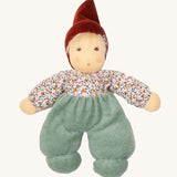 Nanchen Forest Child Waldorf Doll - Sage. This beautifully handcrafted doll wears sage velour trousers, a brown hat and a floral top. On a cream background