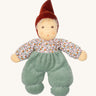 Nanchen Forest Child Waldorf Doll - Sage. This beautifully handcrafted doll wears sage velour trousers, a brown hat and a floral top. On a cream background