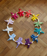 A collection of Hand crafted Nanchen Pimpel Dolls, arranged in a circle on wooden flooring. The colours resemble the rainbow