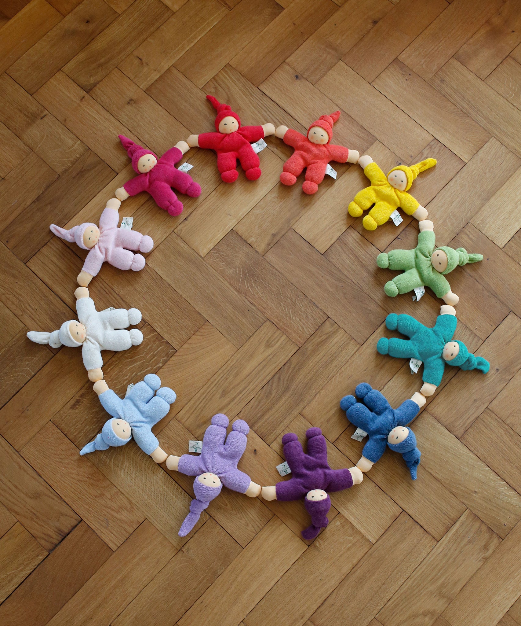 A collection of Hand crafted Nanchen Pimpel Dolls, arranged in a circle on wooden flooring. The colours resemble the rainbow