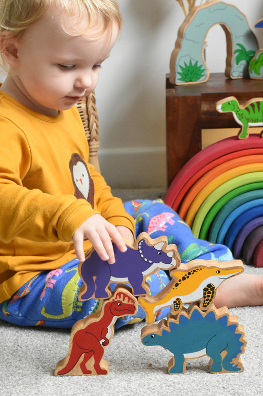 Baby in yellow top stacking chunky Lanka Kade wooden dinosaur figures to represent new Lanka Kade at Babipur, official UK stockist.