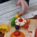 Close up of a child's hand spinning teh carousel top on the Nic Wooden Baby Game busy Board with 4 four activities. 