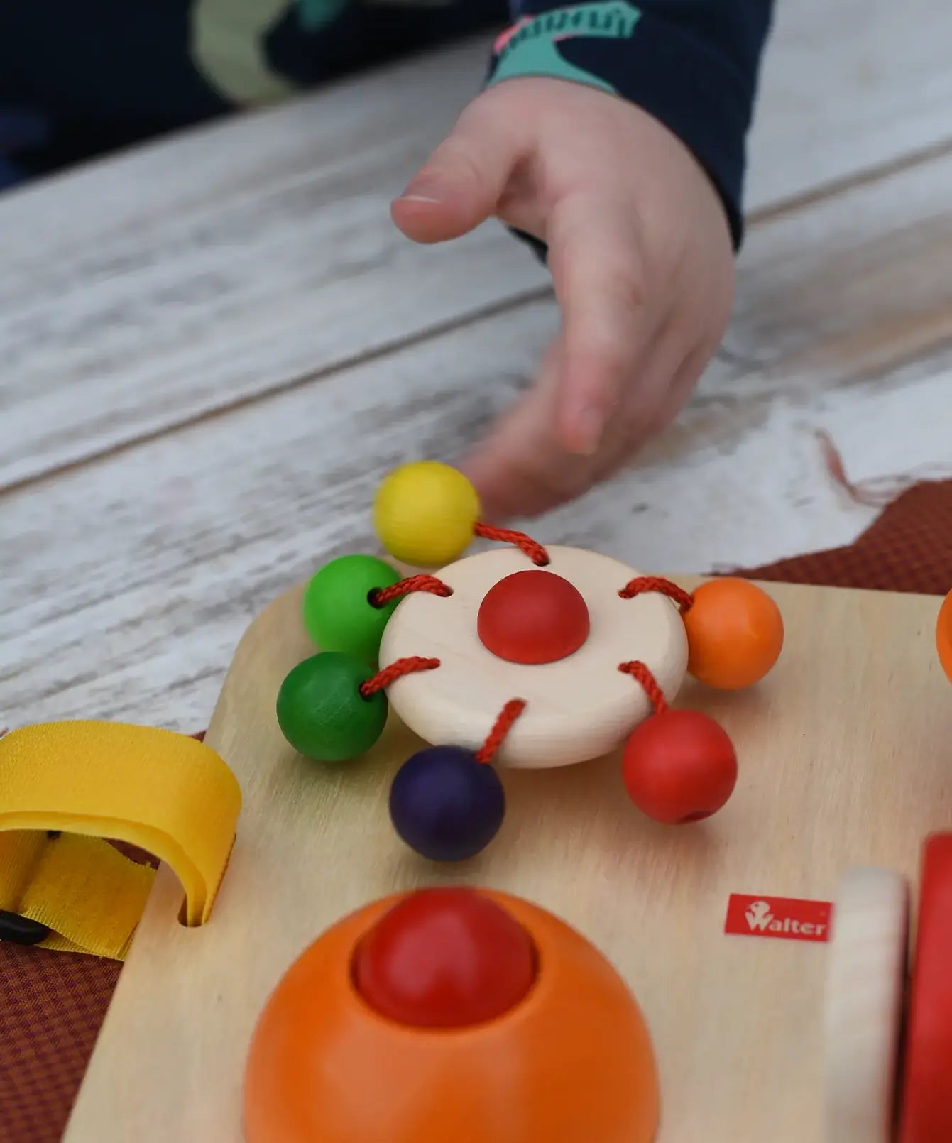 Close up of a child's hand spinning teh carousel top on the Nic Wooden Baby Game busy Board with 4 four activities. 