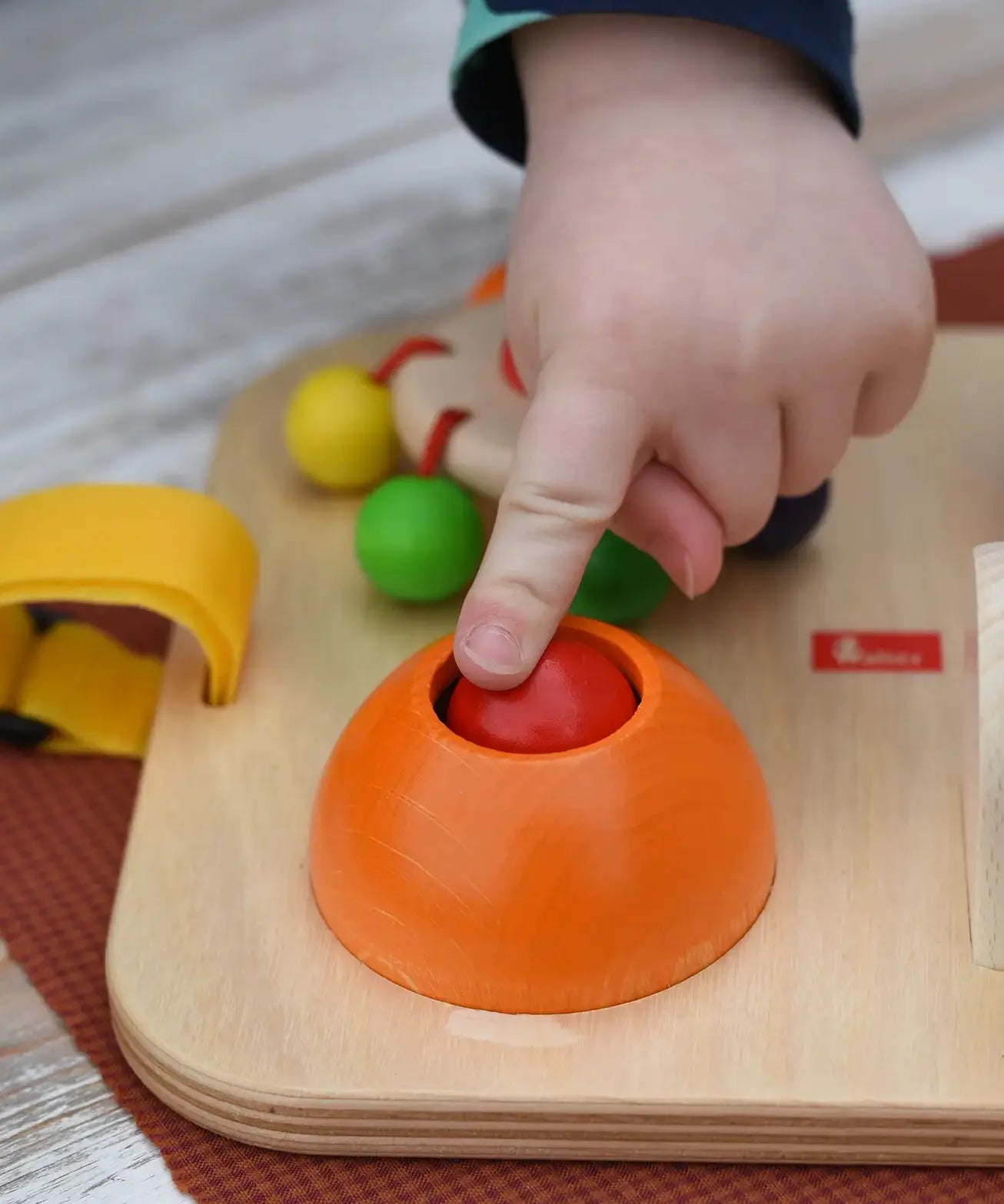 Close up of a child's hand pressing the squeak button on the Nic Wooden Baby Game busy Board with 4 four activities.