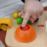 Close up of a child's hand pressing the squeak button on the Nic Wooden Baby Game busy Board with 4 four activities.