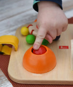 Close up of a child's hand pressing the squeak button on the Nic Wooden Baby Game busy Board with 4 four activities.