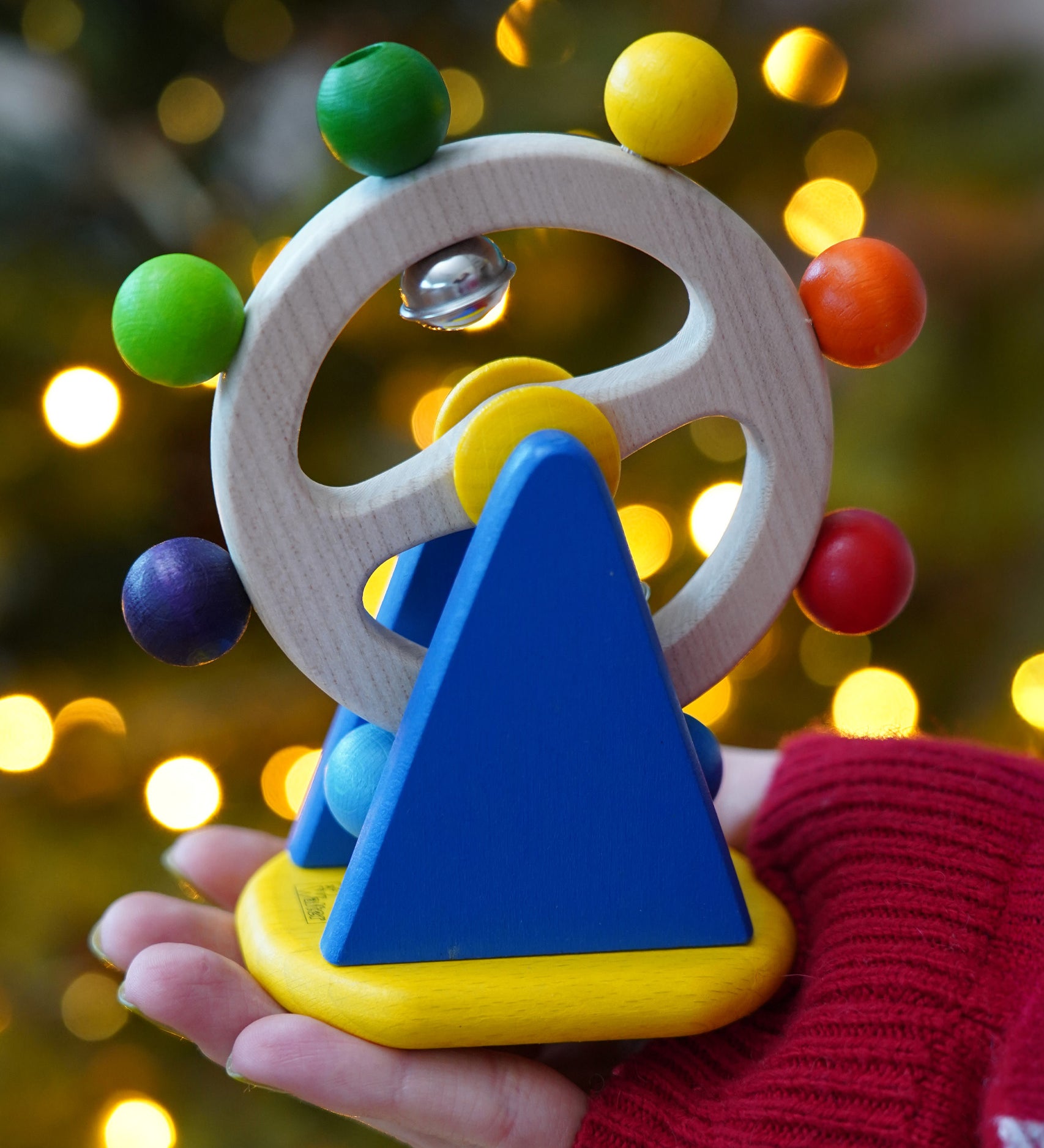 Baby wooden sensory toy, Nic Ferris Wheel, a chunky bright blue stand holding a rotating wheel dotted with rainbow coloured beads and bells, for sale at Babipur.