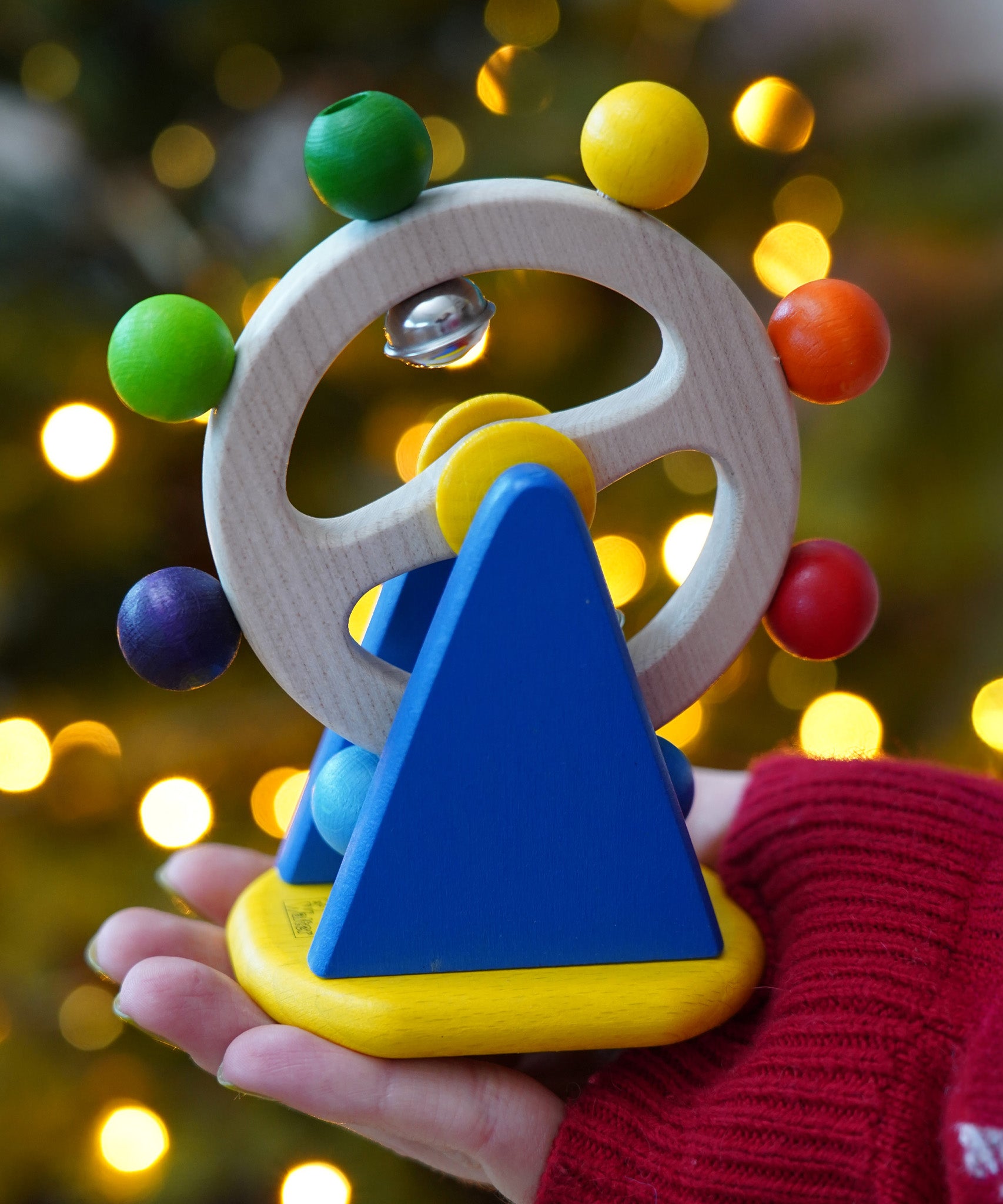 Baby wooden sensory toy, Nic Ferris Wheel, a chunky bright blue stand holding a rotating wheel dotted with rainbow coloured beads and bells, for sale at Babipur.