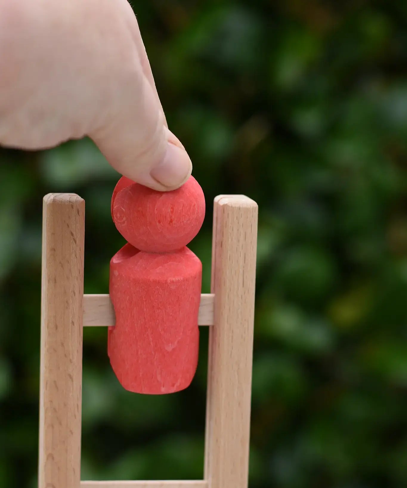 Close up of the Nic climbing wooden ladder toy with a small red peg person being placed on the top ring.
