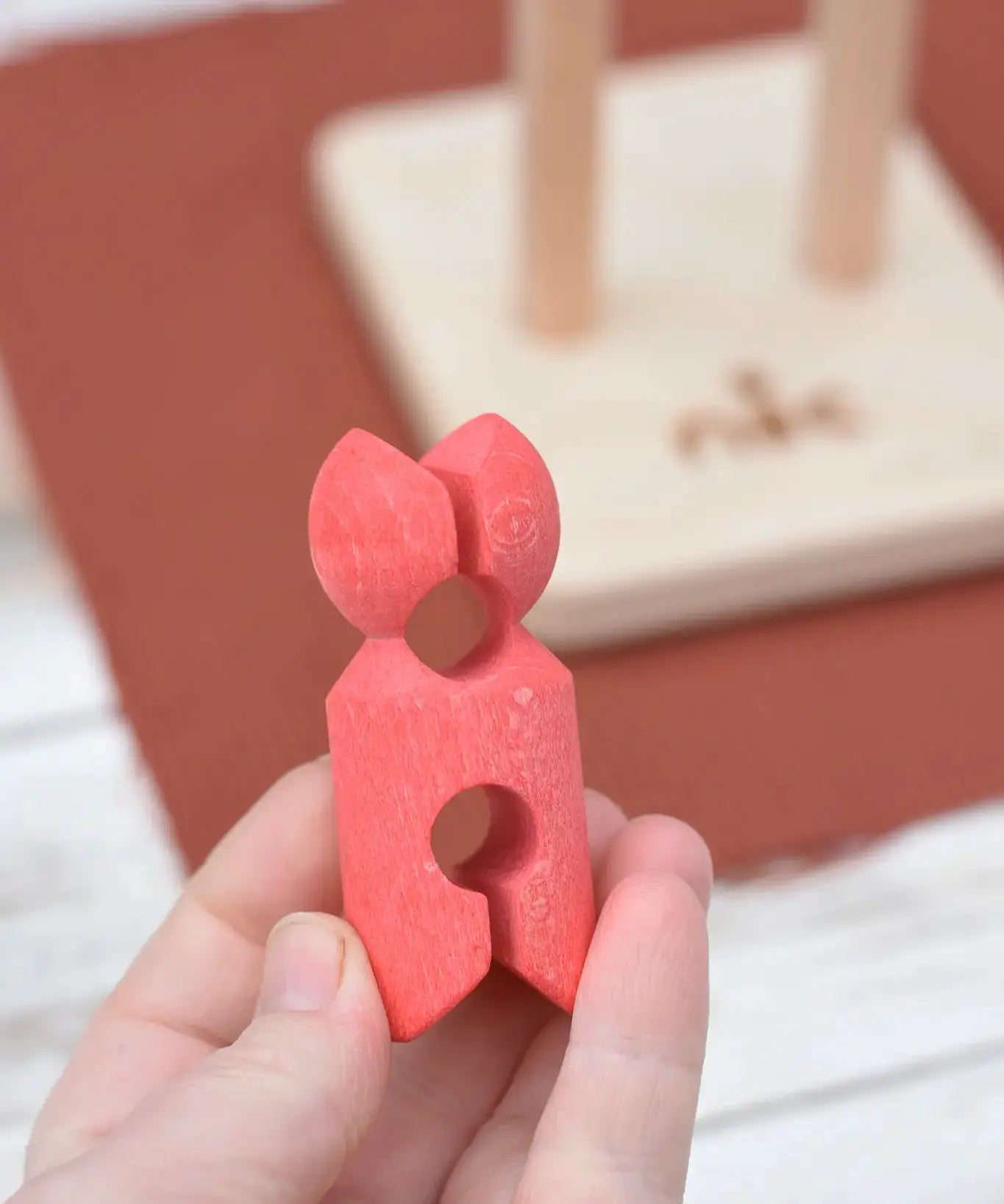 Red peg doll figure from the Nic climbing wooden ladder toy in a adult's hand.