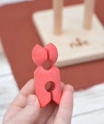 Red peg doll figure from the Nic climbing wooden ladder toy in a adult's hand.