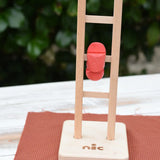 Close up of the Nic climbing wooden ladder toy in action. The red peg doll figure can be seen tumbling down the ladder rungs. 
