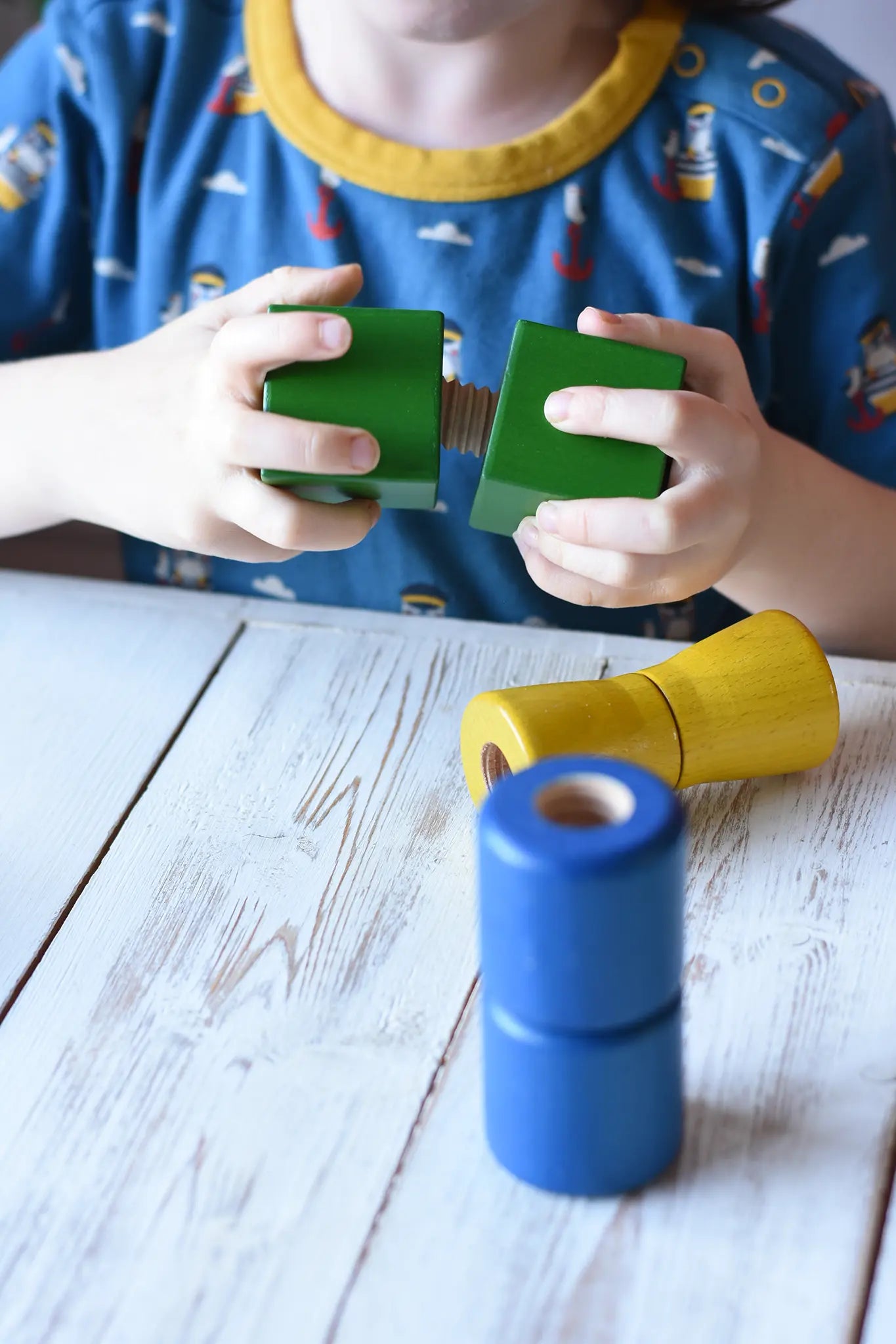 Child screwing two green wooden blocks together from the Nic screws and nuts colorful wooden toy threaded blocks and shapes set.