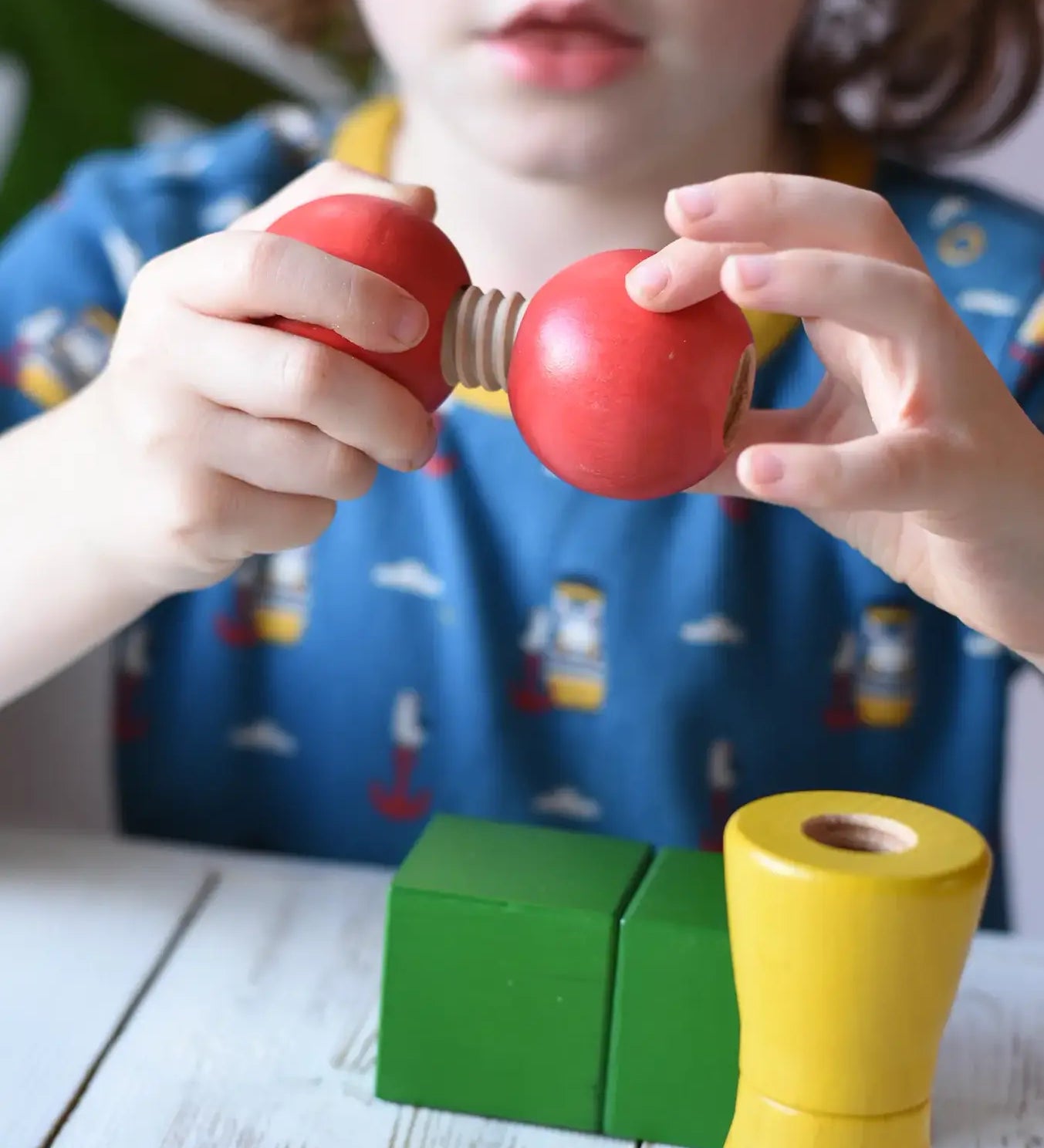 Child threading the two red wooden toy balls one with a thread connector from the Nic screws and nuts colorful wooden toy threaded blocks and shapes.