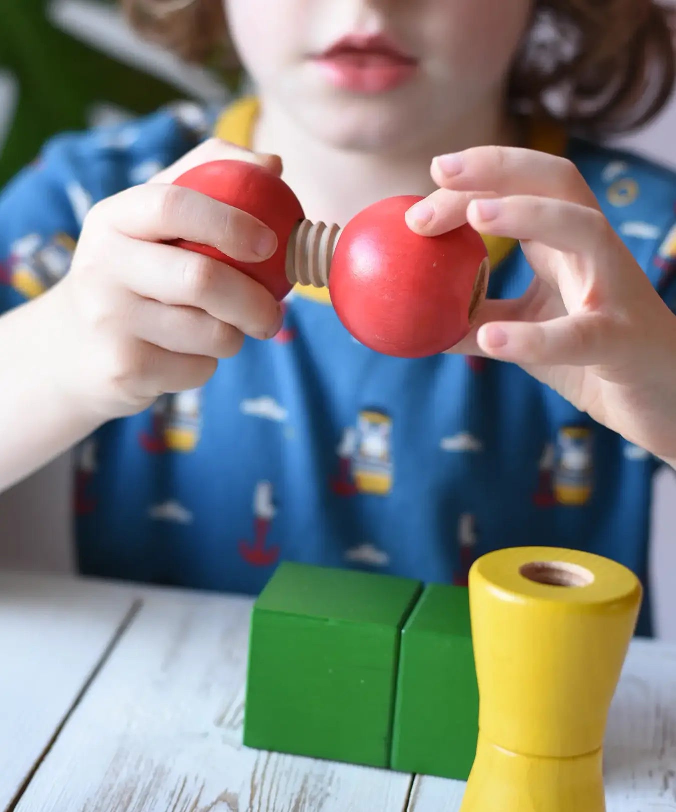 Child threading the two red wooden toy balls one with a thread connector from the Nic screws and nuts colorful wooden toy threaded blocks and shapes.
