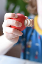 Close-up of a child's hand holding a red, ball-shaped wooden screw from the Nic screws and nuts colorful wooden toy threaded blocks and shapes set.