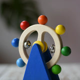 Nic Toys ferris wheel colorful wooden toy for infants and toddlers, featuring a natural wood wheel with colorful painted balls, two silver metal balls, and a blue triangular support on a yellow base, set on a light wooden tabletop.