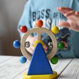 Nic Toys ferris wheel colorful wooden spinning toy, child's hand reaching for it in the background.