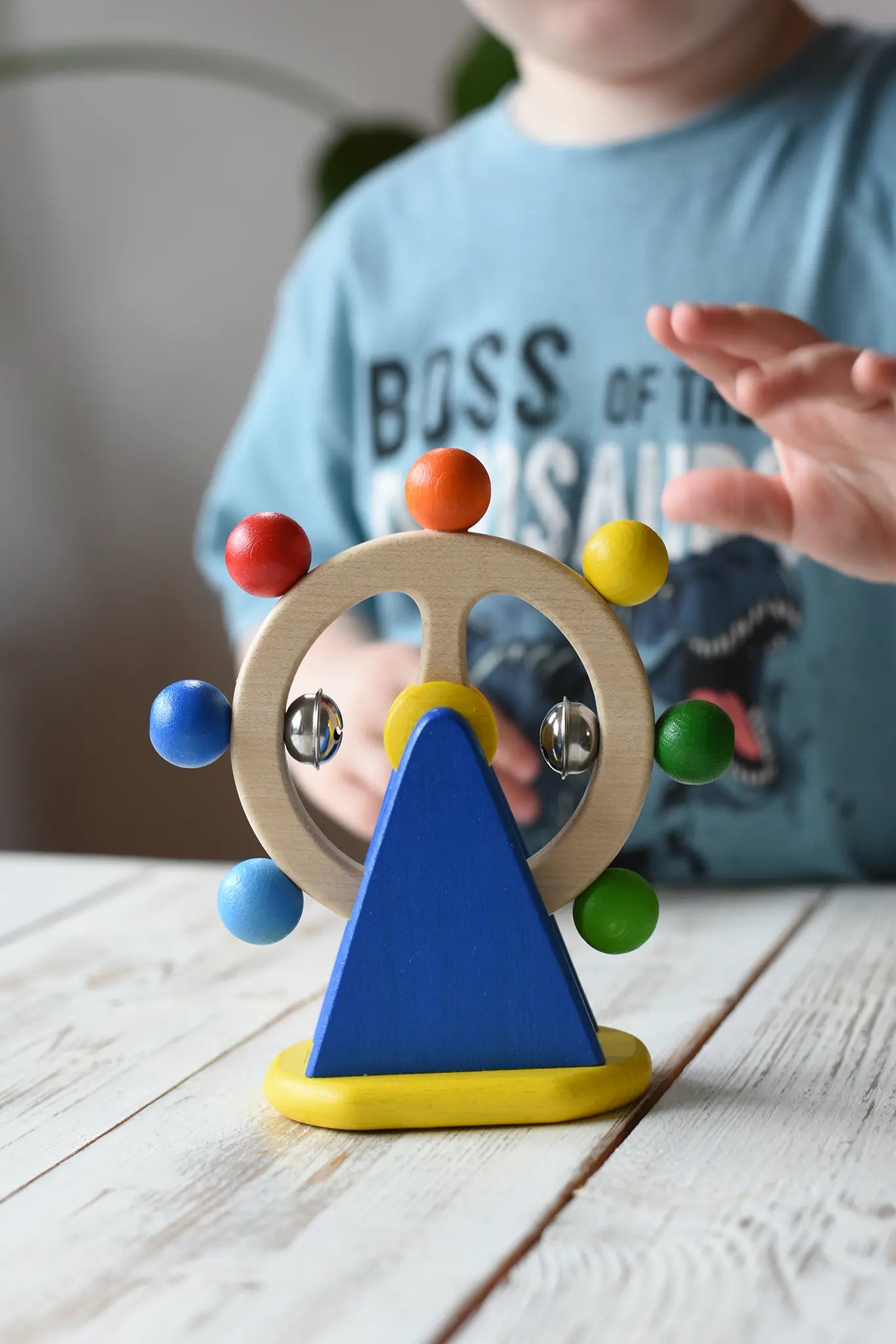 Nic Toys ferris wheel colorful wooden spinning toy, child's hand reaching for it in the background.