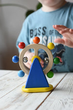 Nic Toys ferris wheel colorful wooden spinning toy, child's hand reaching for it in the background.