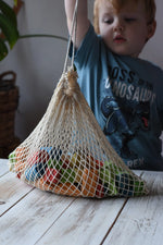 Child lifting a net bag filled with Glückskäfer Wooden Bio Geometric Building Blocks in a 58 Piece Set.