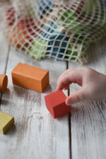 Close up of a child's hand playing with blocks from the Gluckskafer Wooden Bio Geometric Building Blocks 58 Piece Set. 