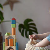 Child taking Glückskäfer Wooden Bio Geometric Building Blocks out of the net storage bag next to a tower created with the blocks.  