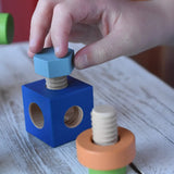 Child's hand threading a srew into a blue blocks from the Nic set of colorful wooden screws and block set. 