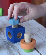 Child's hand threading a srew into a blue blocks from the Nic set of colorful wooden screws and block set. 
