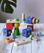 Nic set of colorful wooden screws and blocks arranged wooden tabletop, with a blurred green plant leaf in the background.