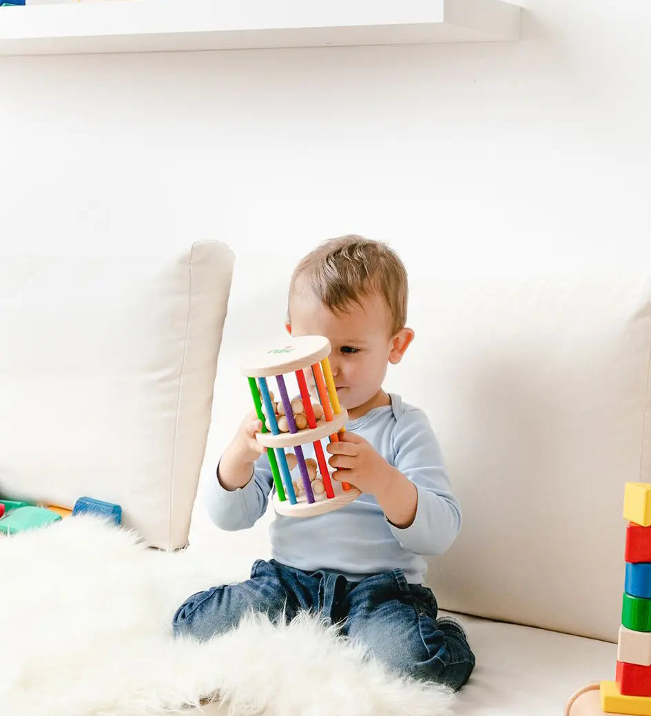 Nic Toys Rattle n Roll - a young child holding and playing with a natural wooden rolling toy with rainbow stained rungs and wooden marbles.