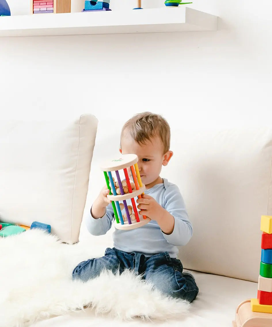 Nic Toys Rattle n Roll - a young child holding and playing with a natural wooden rolling toy with rainbow stained rungs and wooden marbles.