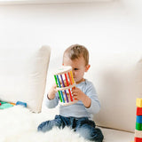 Nic Toys Rattle n Roll - a young child holding and playing with a natural wooden rolling toy with rainbow stained rungs and wooden marbles.