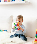 Nic Toys Rattle n Roll - a young child holding and playing with a natural wooden rolling toy with rainbow stained rungs and wooden marbles.