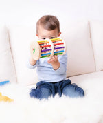 Nic Toys Rattle n Roll - a child playing with a colourful wooden baby toy made with rainbow stained rungs and natural wooden marbles.