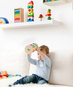 Nic Toys Rattle n Roll - a wooden musical rolling wheel toy for babies, shown with its natural finish, rainbow rungs and wooden marbles in a playroom setting.