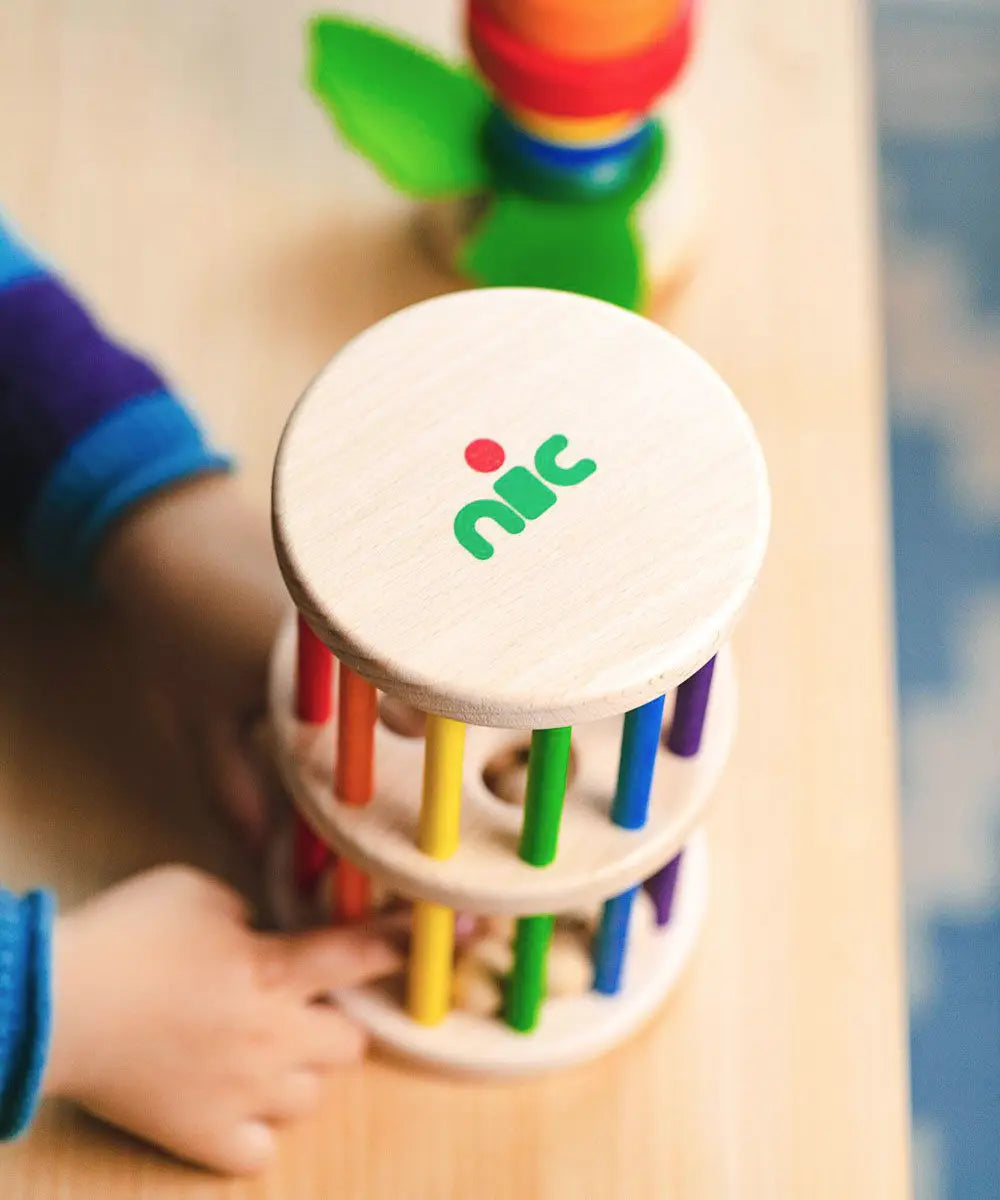 Nic Toys Rattle n Roll - a child playing with the wooden rolling wheel musical toy, which has rainbow stained rungs and wooden marbles.
