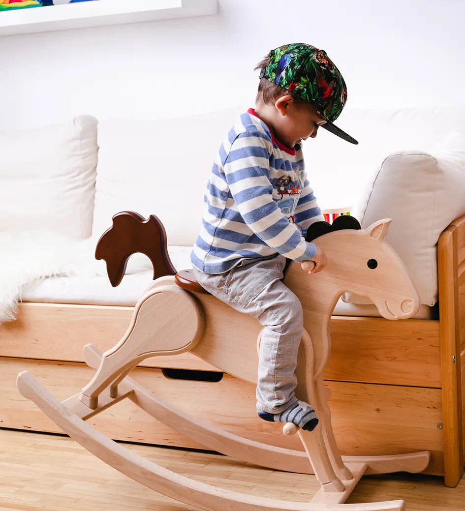 Nic Toys Wooden Rocking Horse with natural finish and brown painted mane, seat and tail, being played with by child in a bedroom.