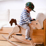 Nic Toys Wooden Rocking Horse with natural finish and brown painted mane, seat and tail, being played with by child in a bedroom.