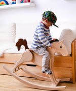 Nic Toys Wooden Rocking Horse with natural finish and brown painted mane, seat and tail, being played with by child in a bedroom.