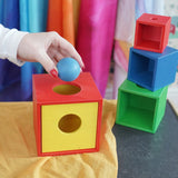Nic Toys Stacking boxes set. A hand  places a blue ball into the  red and yellow wooden box put togethr like a  shape-sorting box. 