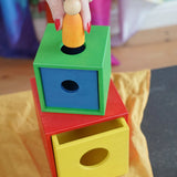 A colorful Nic Toys wooden stacking and nesting box toy with a being used as a permanence box to insert a small wooden peg doll.