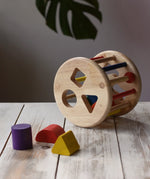 Nic rolling sorter wooden shape-sorting toy with colorful geometric blocks, displayed on a wooden table.