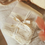 Avery Row Stripe Knit Organic Baby Blanket - Oat Melange, folded with branded ribbon on a changing table. 