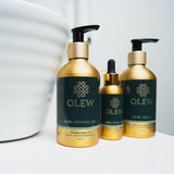 The Olew Curl Defining Gel, Original Oil and Curl Cream in gold and dark green bottles, stood on a white table with a white large bowl next to the bottles.