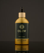 Olew Hold Spray - Curl Keeper, giving natural hold and shine. Vegan haircare which is SLS and Paraben Free, in a gold and dark green bottle with a spray mist pump on top. The image is on a dark grey background